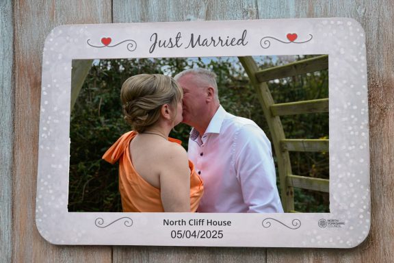 A newlywed couple sharing a kiss in a rustic frame. Wedding date and location displayed.