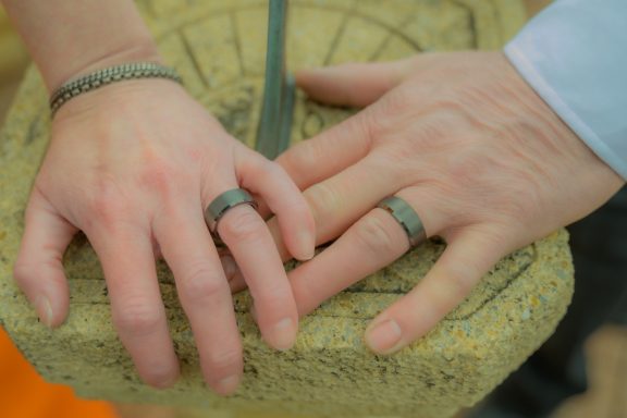 Two hands with rings resting on a textured stone surface.