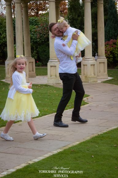 A man carries a girl in a yellow dress, while another girl in a similar dress walks nearby.