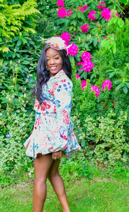 Woman in a floral dress stands among vibrant pink flowers in a lush garden.